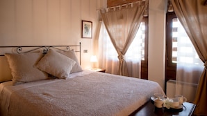 Cama bem arrumada com cabeceira, mesa de cabeceira com abajur e cortinas.