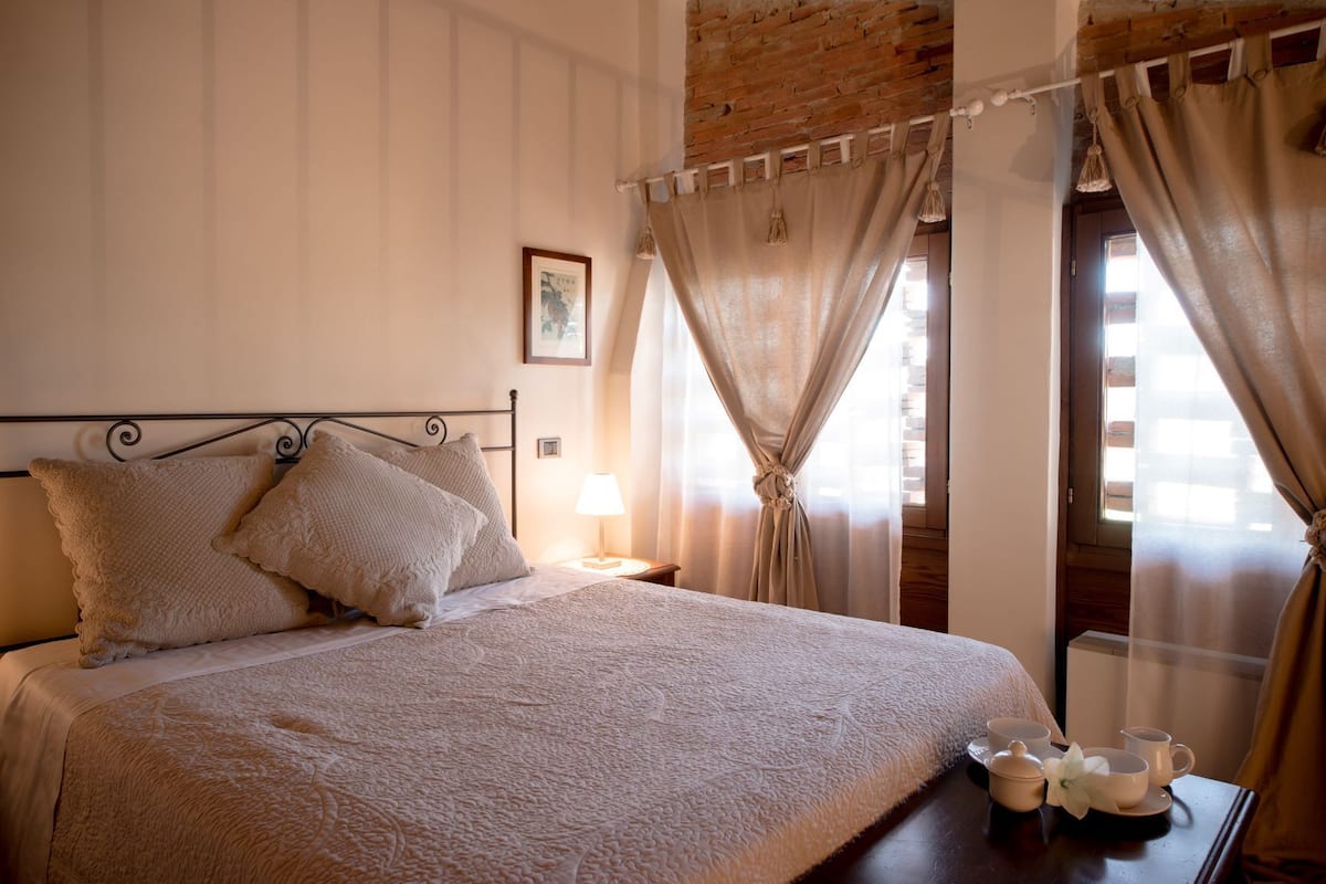 Una cama bien hecha con cabecera, una mesita de noche con lámpara y cortinas.