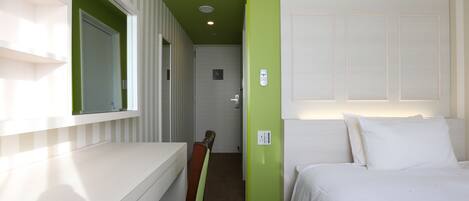 A hotel room with a white bed, green walls, a white desk, and a mirror.