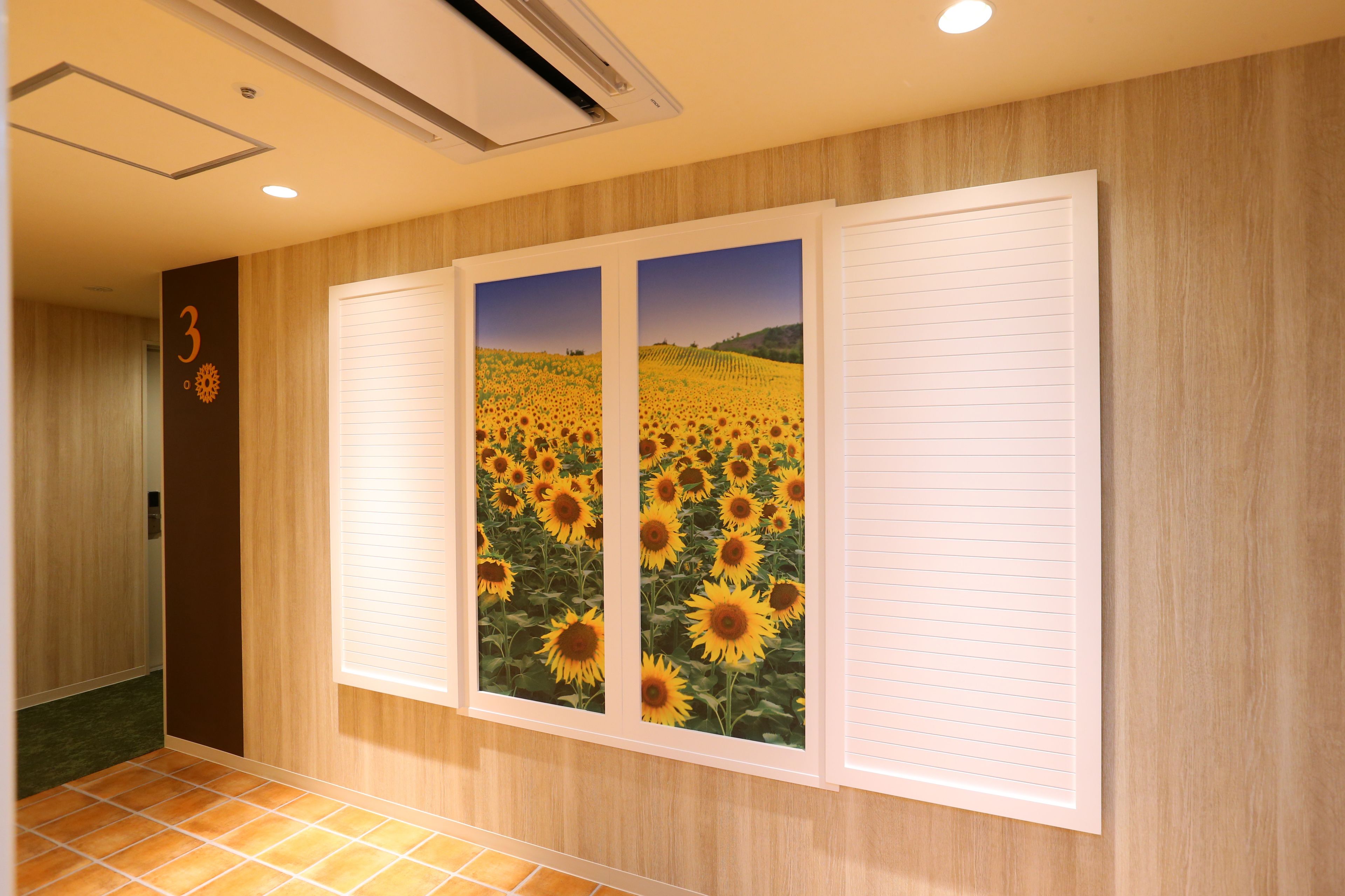 A hallway with wooden paneling, a door marked with the number 3, and two large framed pictures of sunflowers.