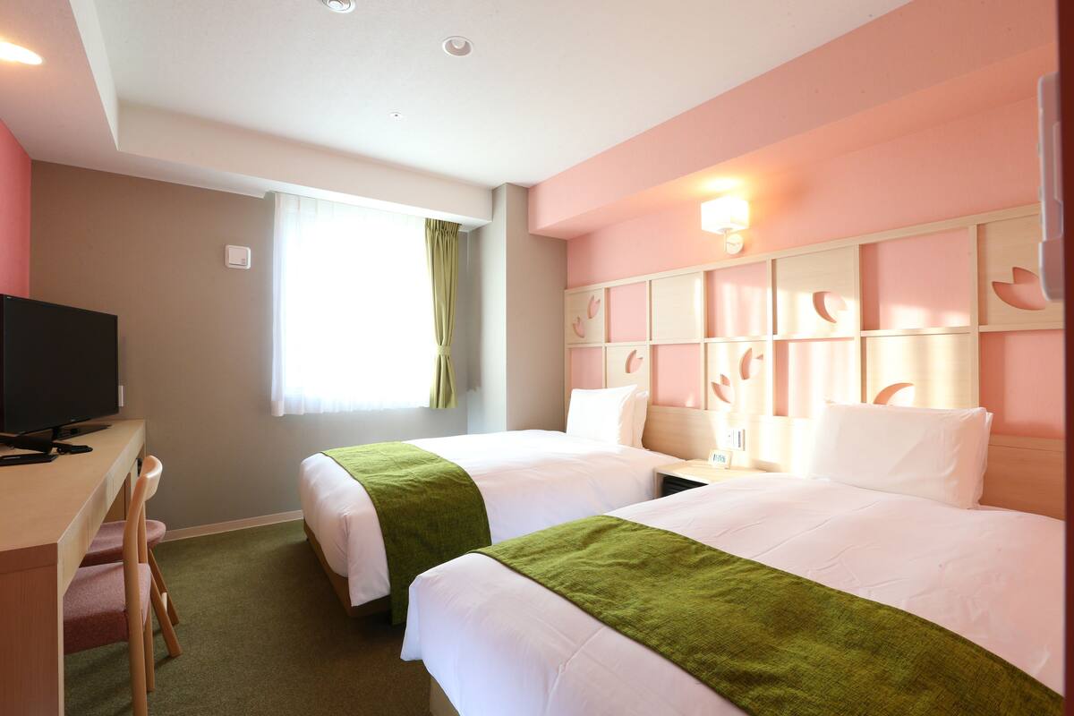 Ein Hotelzimmer mit zwei Betten, einem Schreibtisch und einem Fernseher.