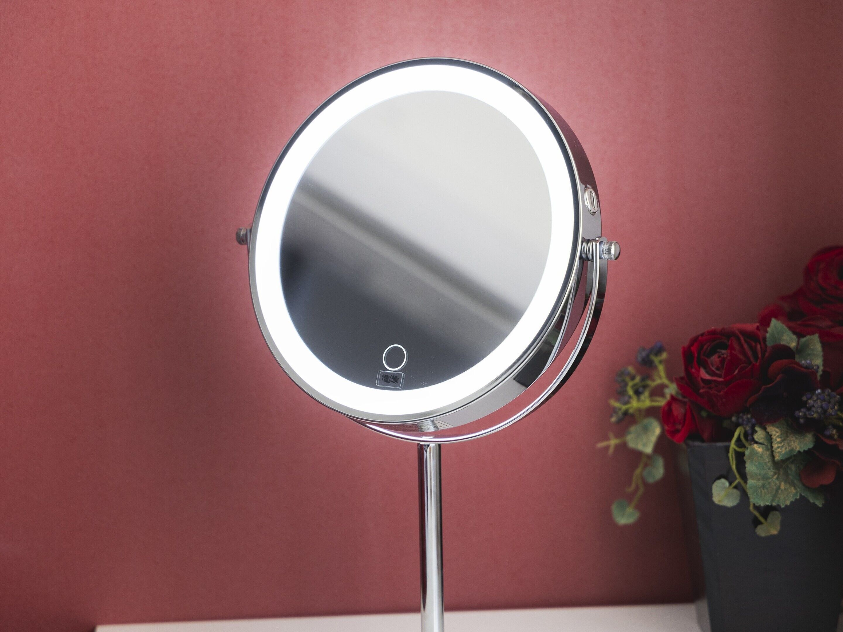 Un miroir rond doté d’un cadre lumineux, placé sur un fond rouge.