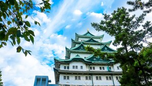 Eine traditionelle japanische Burg mit mehreren Ebenen und grünen Dächern, umgeben von Bäumen und wolkenlosem Himmel.