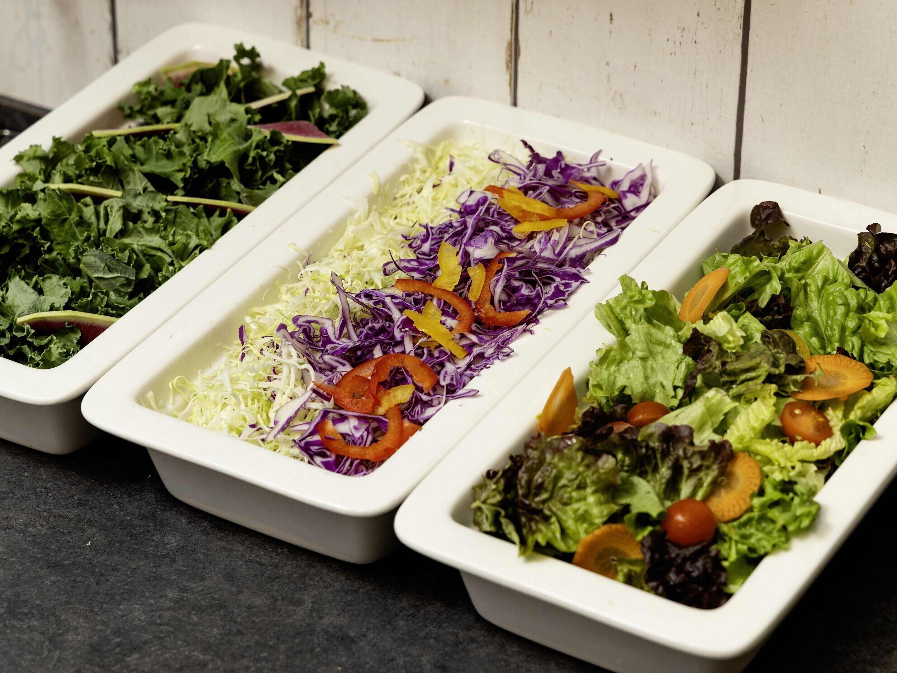 Three white rectangular trays containing different salads with various vegetables.