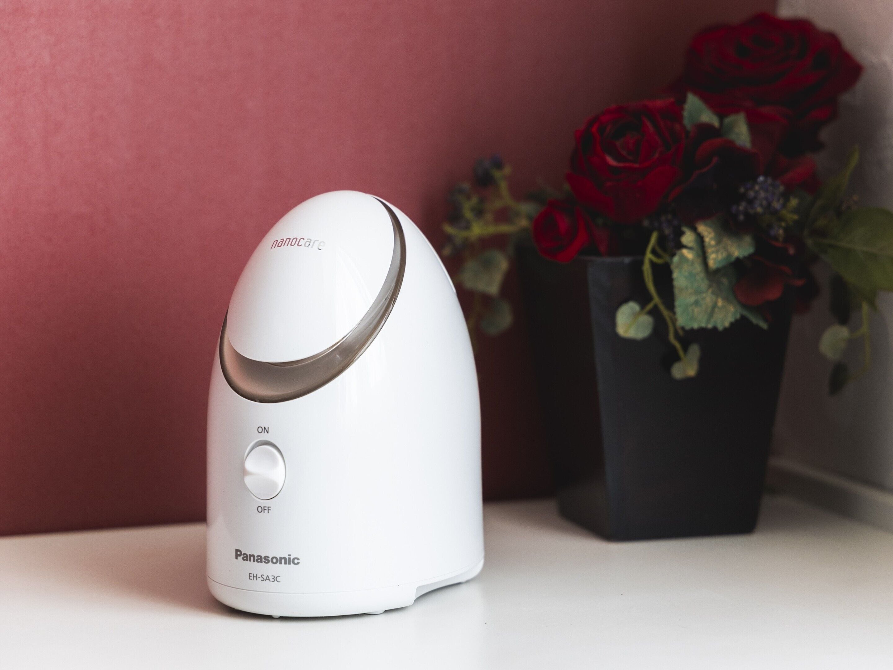 A white Panasonic EH-SA3C device with an on/off switch, placed on a surface next to a vase with red roses.