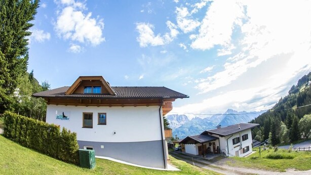En toetagers chalet med skråt tag, garage og udsigt til bjerge i baggrunden.