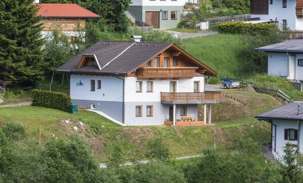 A two-story house with a balcony, surrounded by greenery and other houses.