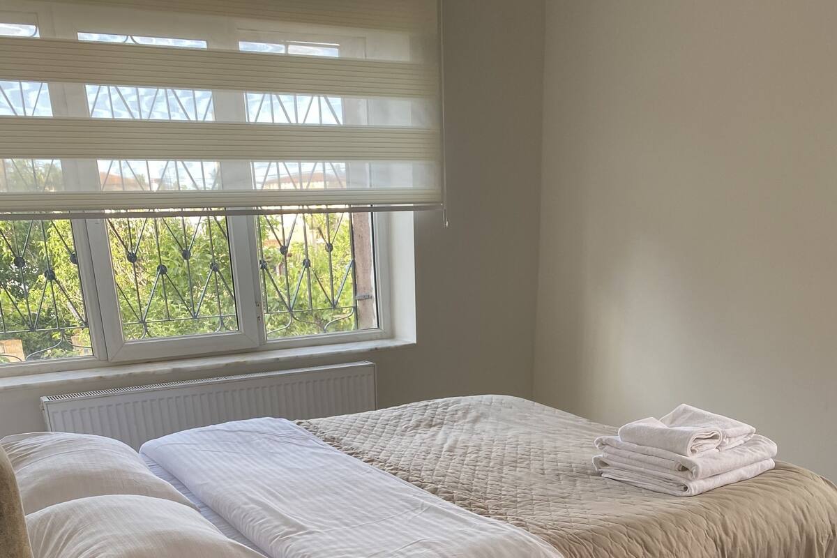 A bedroom with a bed, a radiator, a window with blinds, and a checkered rug.