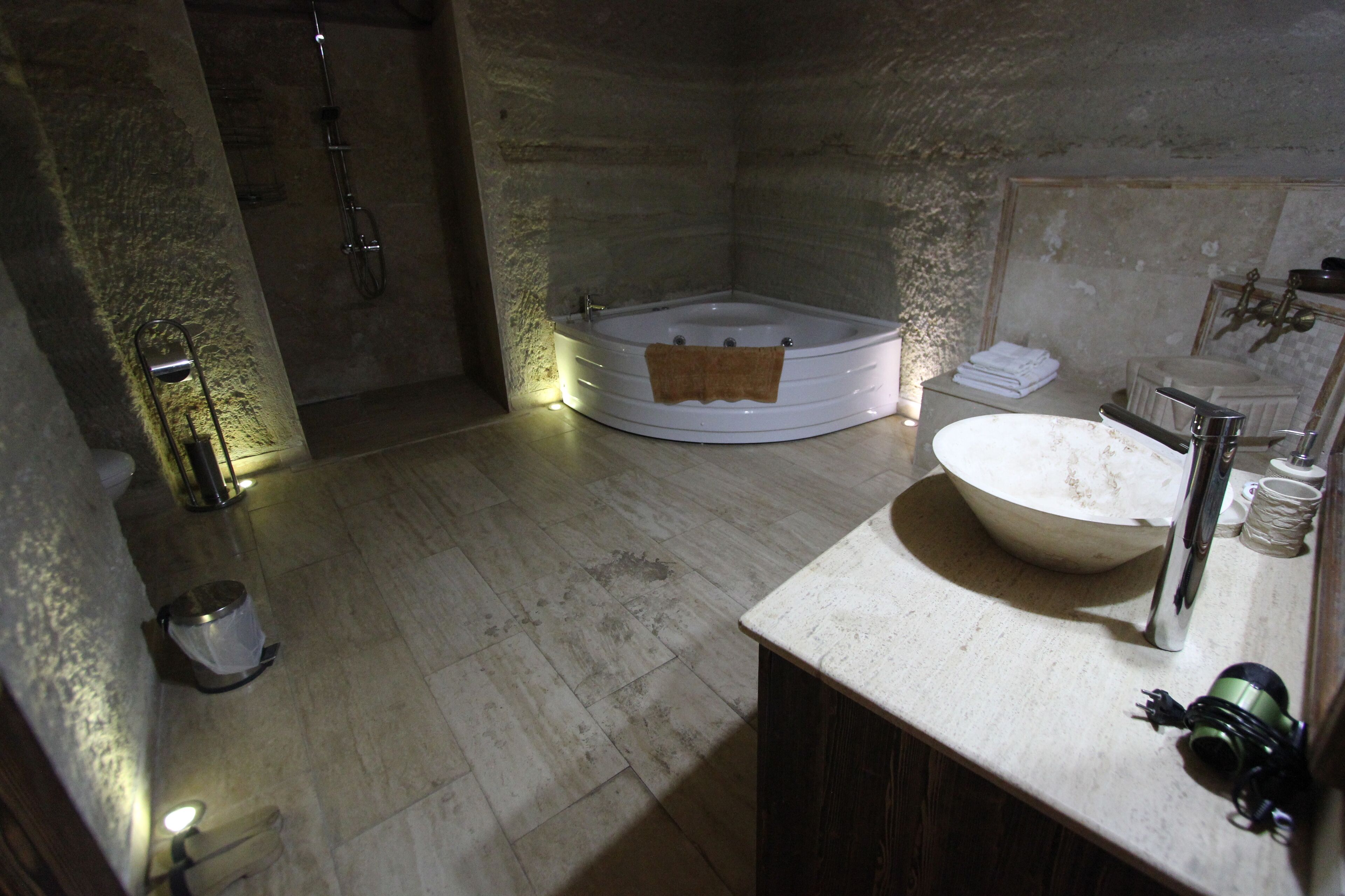 A bathroom with a bathtub, a sink, and a toilet. There are towels stacked on the sink and a trash bin next to the toilet.