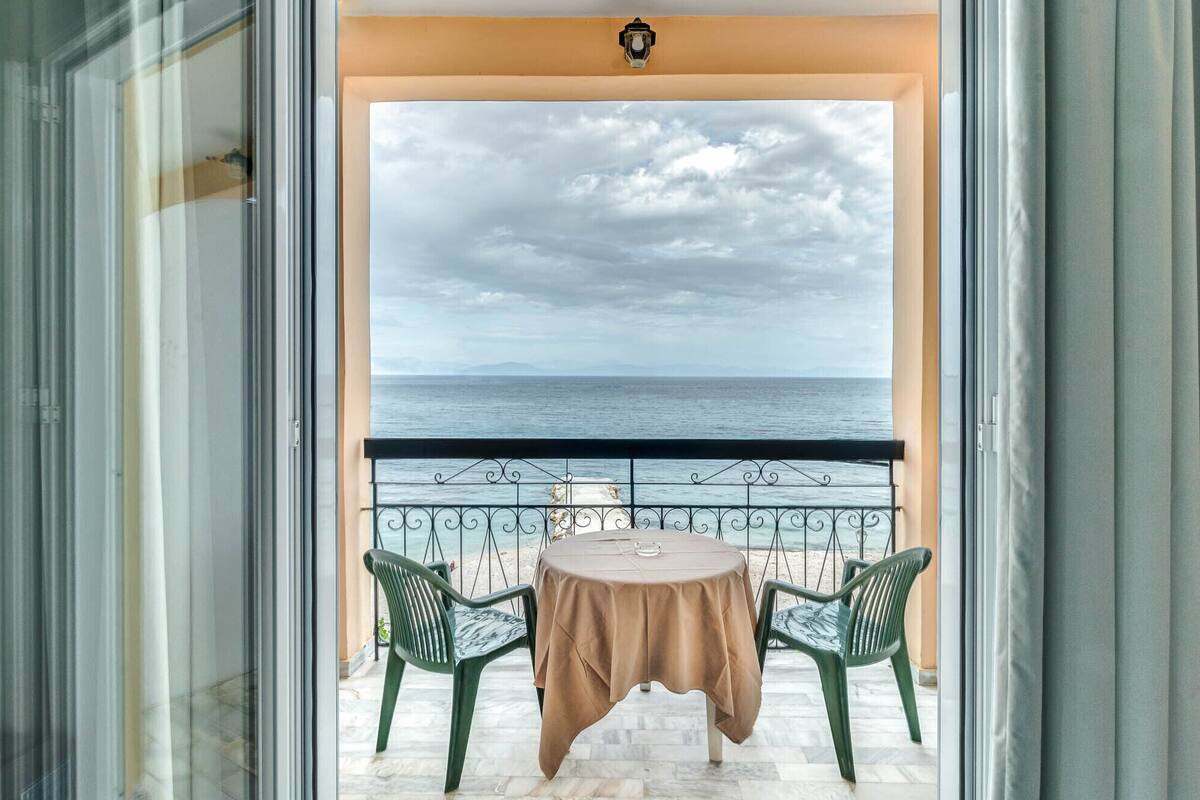A balcony with a table and two chairs, overlooking a body of water and distant land.