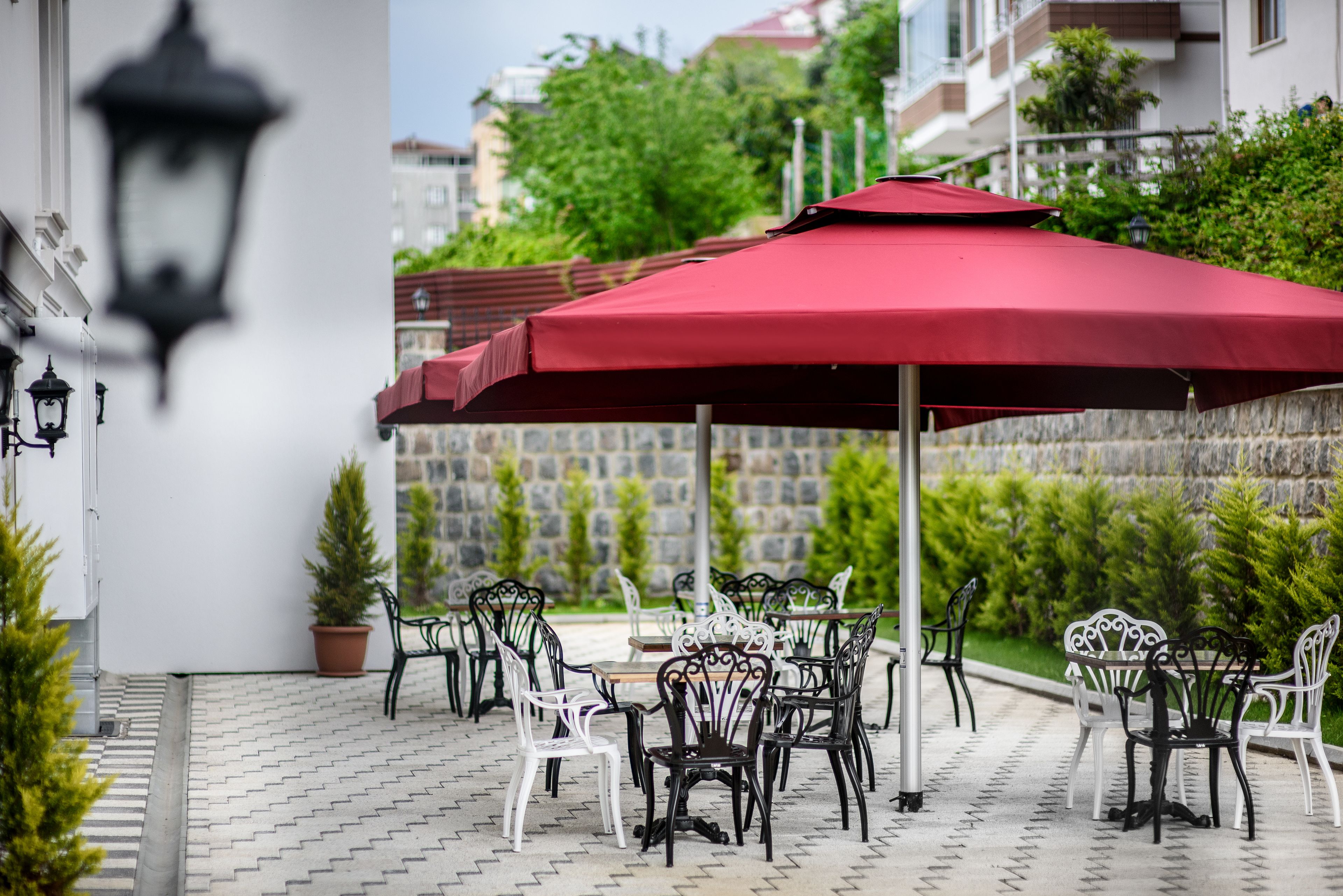 An outdoor seating area with tables and chairs, a red umbrella, and potted plants.