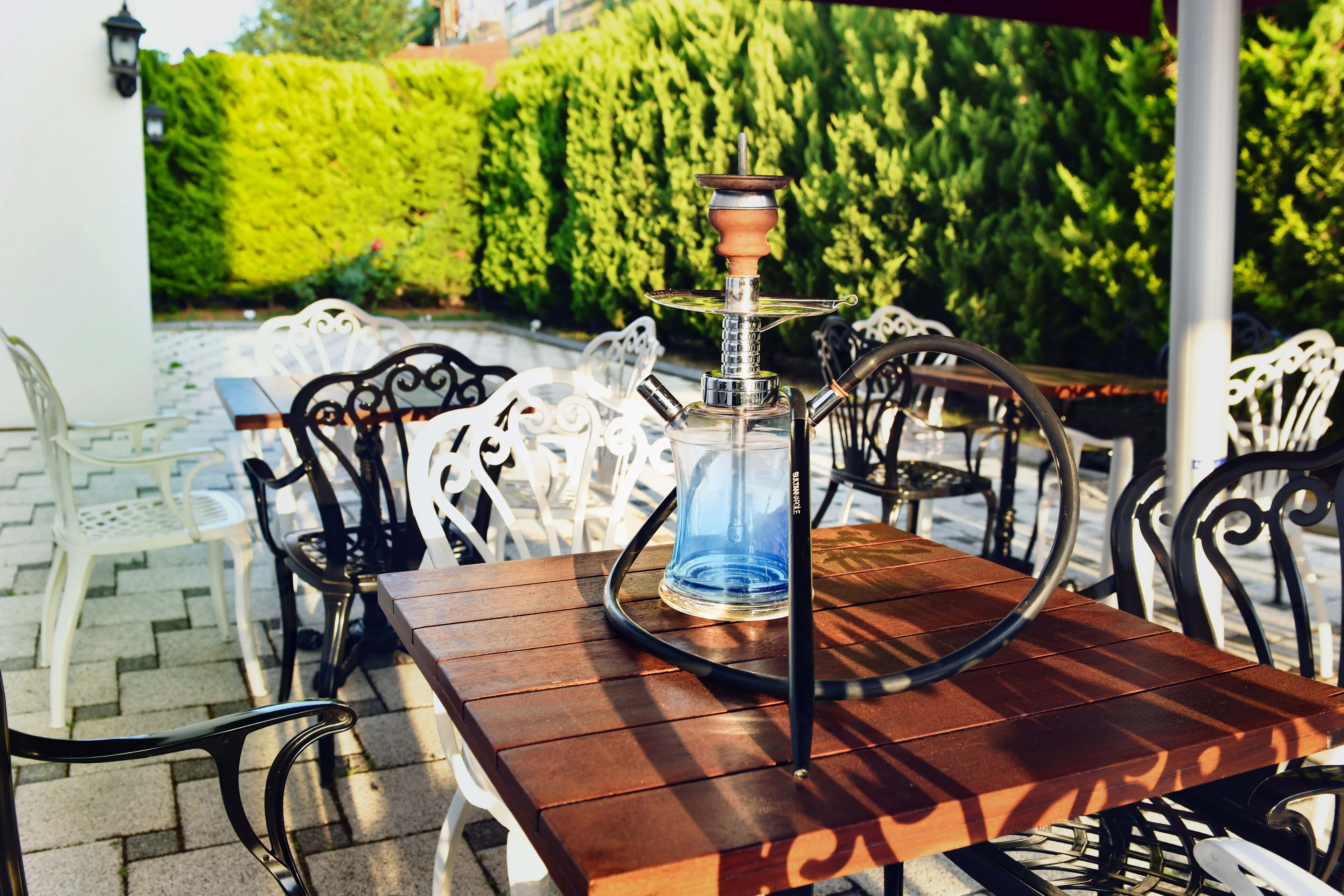 A wooden table with a hookah on it, surrounded by white metal chairs.
