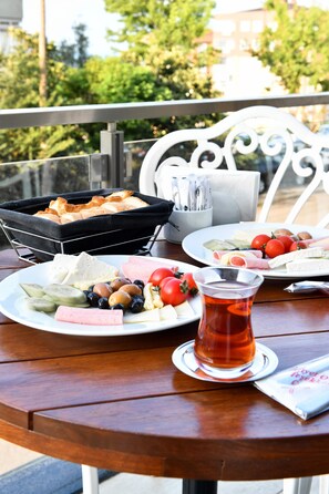 A table with a variety of food items including bread, cheese, tomatoes, cucumbers, and olives, along with a glass of tea. - White House Hotel (Trabzon)