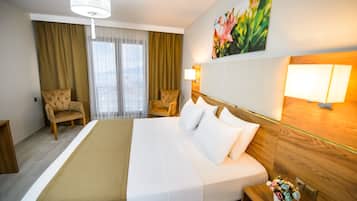 Une chambre d’hôtel avec un grand lit, deux fauteuils, une tête de lit en bois, un lustre, un tableau et une table de chevet ornée d’un vase de fleurs.