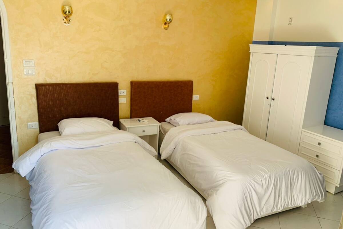 Ein Hotelzimmer mit zwei Einzelbetten, einem Nachttisch, einem Schrank und einer Wandleuchte.