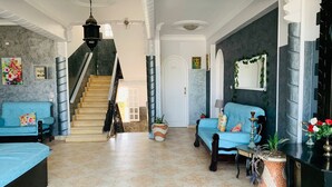 Uma sala de estar ampla com escada, dois sofás azuis, uma mesa de centro e um vaso de planta.