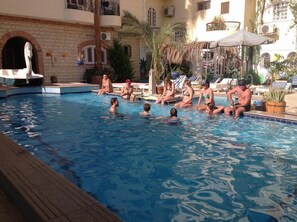 A swimming pool with people relaxing around it, surrounded by buildings with balconies and plants. - Nile Valley Hotel & Restaurant (Luxor)