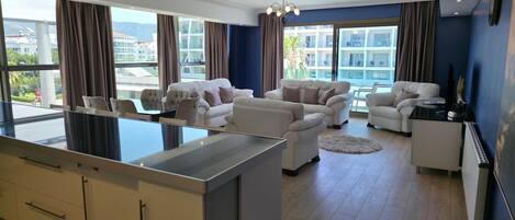 A modern living room with a kitchen area, large windows, and a view of the cityscape.
