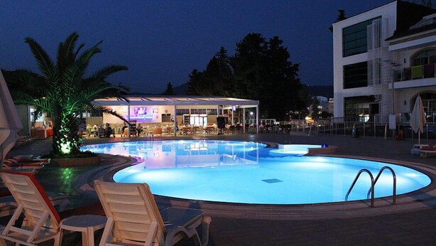 En swimmingpool med liggestole, et barområde og en moderne bygning i baggrunden.