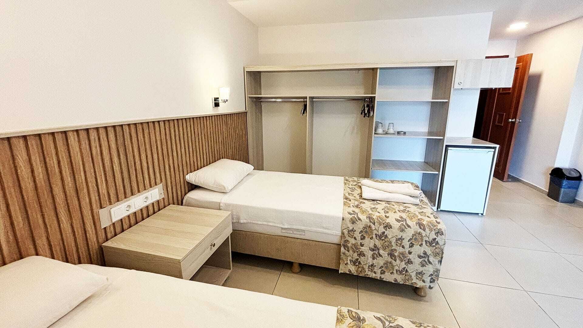 A hotel room with a bed, a small desk, a wardrobe, and a mini-fridge.