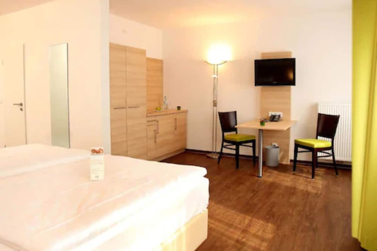 A hotel room with a bed, a desk with two chairs, a TV, and a wardrobe.
