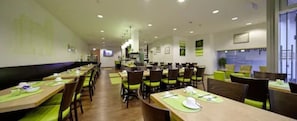 A modern restaurant with long tables, green chairs, and a bright interior.