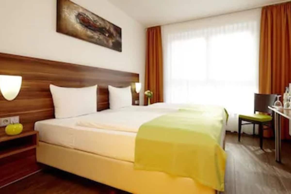 A hotel room with a large bed, a desk, and a chair.