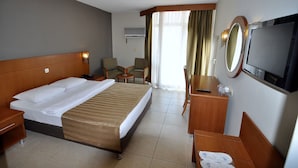 A hotel room with a bed, a desk, a chair, a TV, and a window with curtains. - Surtel Hotel (Kusadasi)