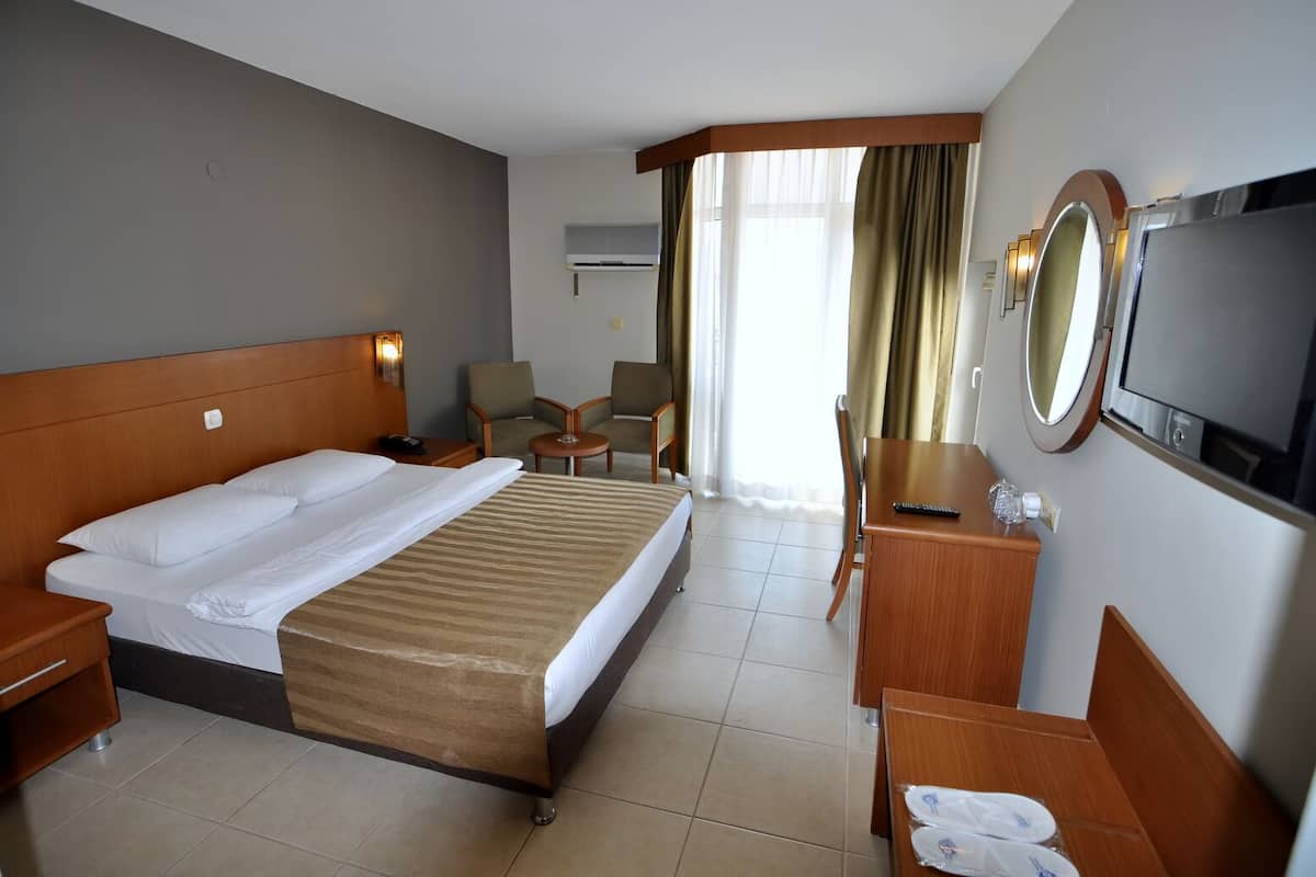 A hotel room with a bed, a desk, a chair, a TV, and a window with curtains.