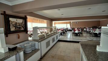 A hotel dining area with a buffet setup, multiple tables, and chairs.