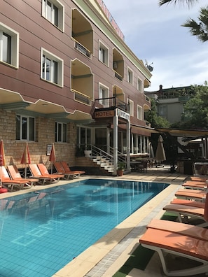 A hotel with a swimming pool, lounge chairs, and a staircase leading to the entrance.