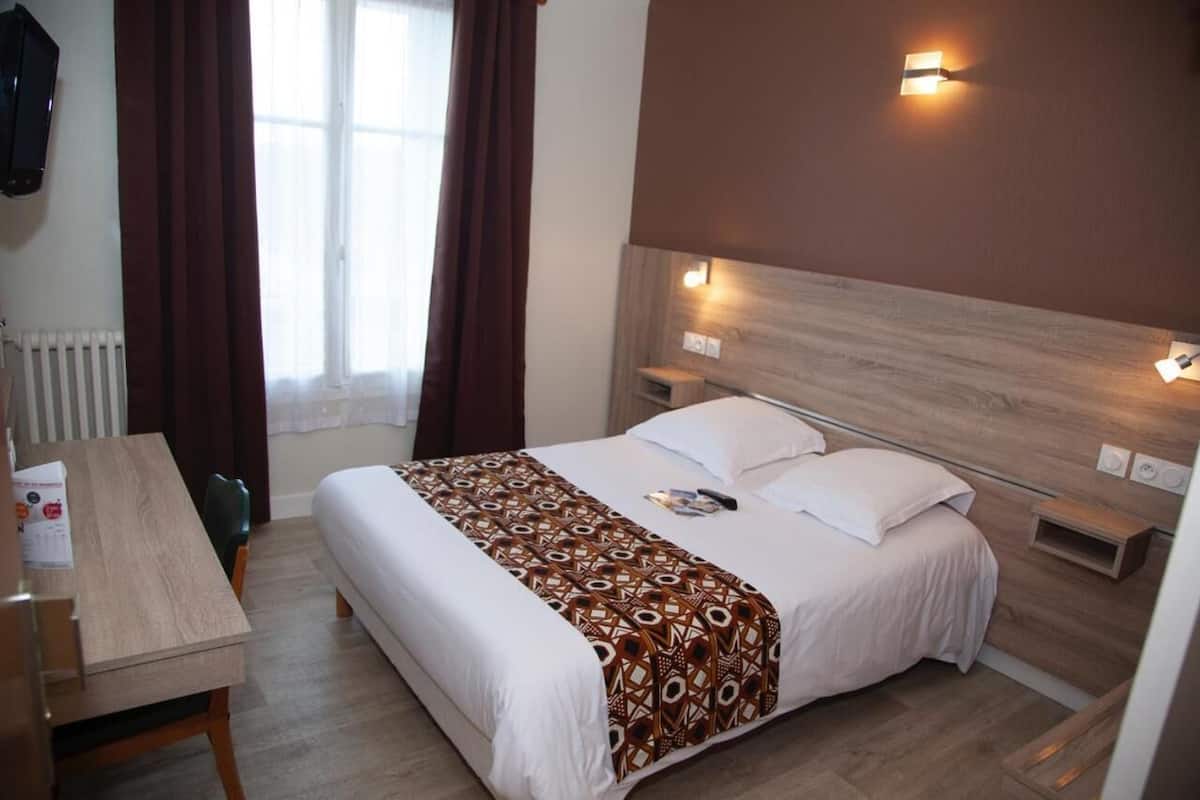 A hotel room with a bed, bedside tables, a desk, and a window with curtains.
