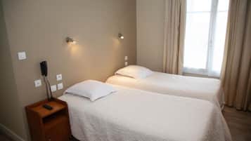 A room with two beds, a nightstand with a phone, and a window with curtains.