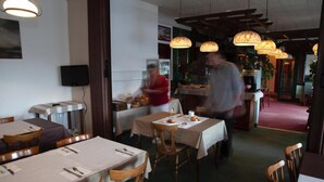 Un restaurante con mesas dispuestas para comer, una zona de bar y una barra con una persona atendiendo.