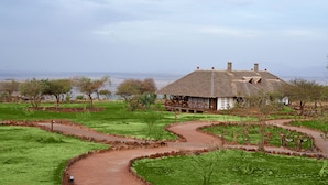 A thatched-roof house with a wooden deck, surrounded by a landscaped garden with pathways. - Lake Manyara Kilimamoja Lodge (Lake Manyara National Park)