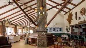 A spacious living area with a stone fireplace, wooden beams, and a bar area with a sign reading "Explorers Bar".