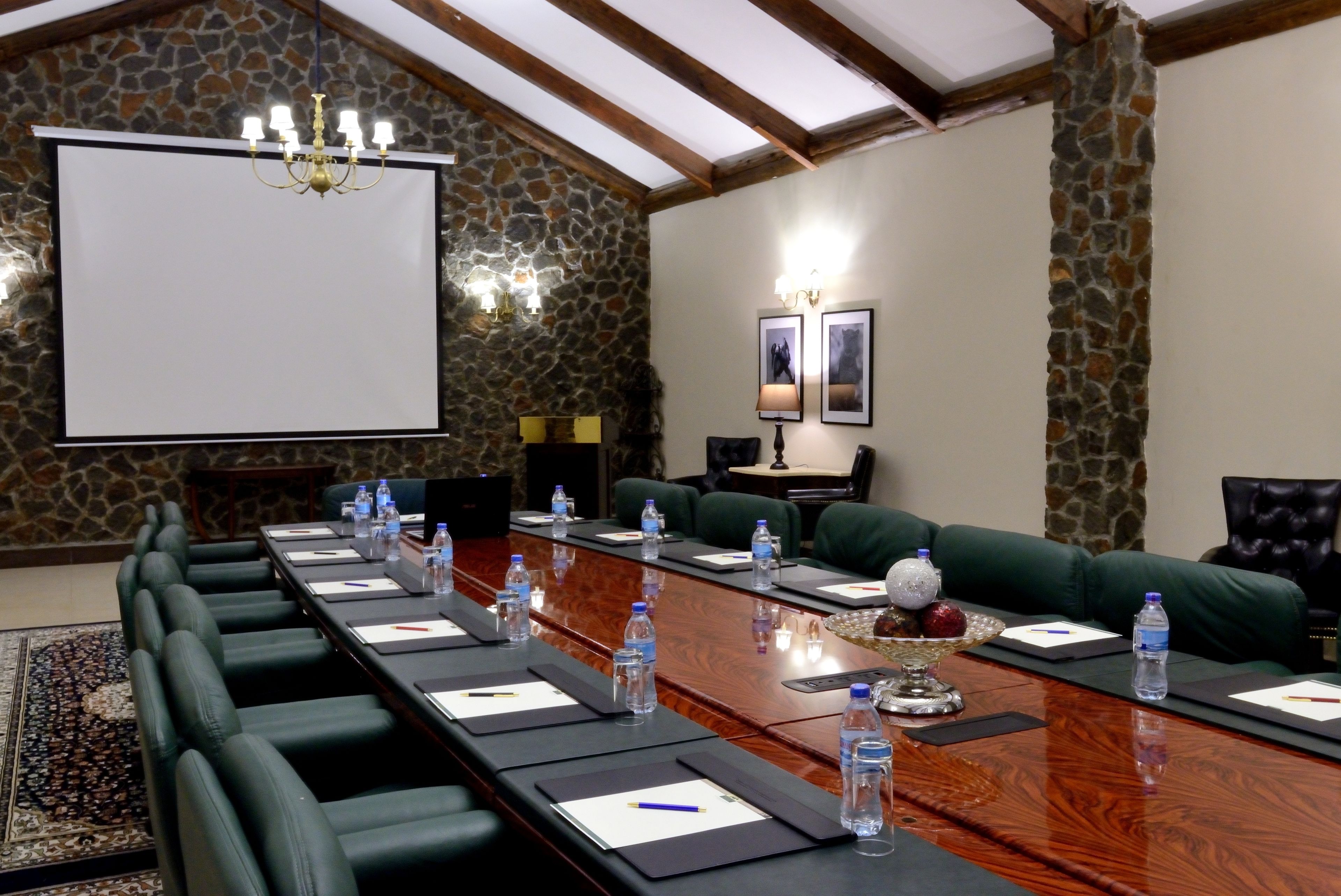 A conference room with a long table, chairs, a projector screen, and a stone wall.