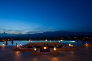 A poolside area with seating and a fire pit, surrounded by candles, overlooking a body of water and mountains. - Ngorongoro Oldeani Mountain Lodge (Karatu)