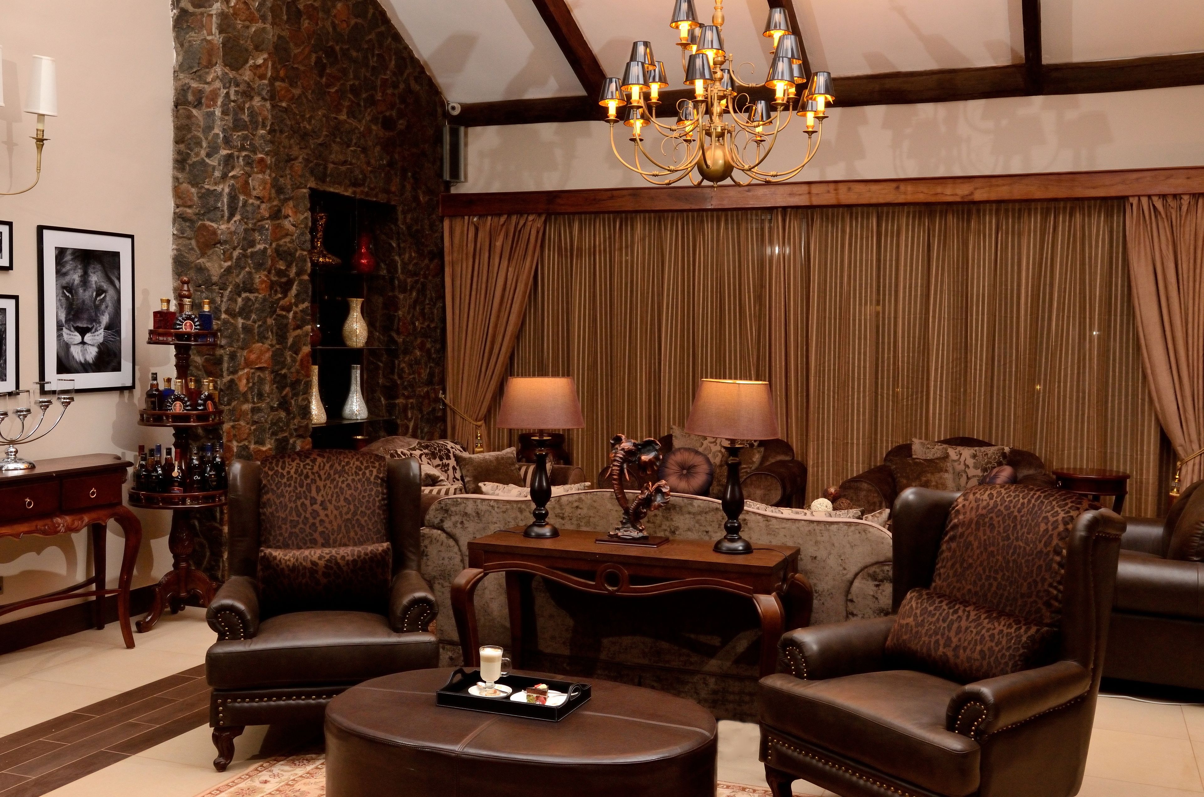 Una sala de estar acogedora con sillones de cuero, una mesita de centro y un candelabro. Hay una chimenea con pared de piedra y un ventanal con cortinas.