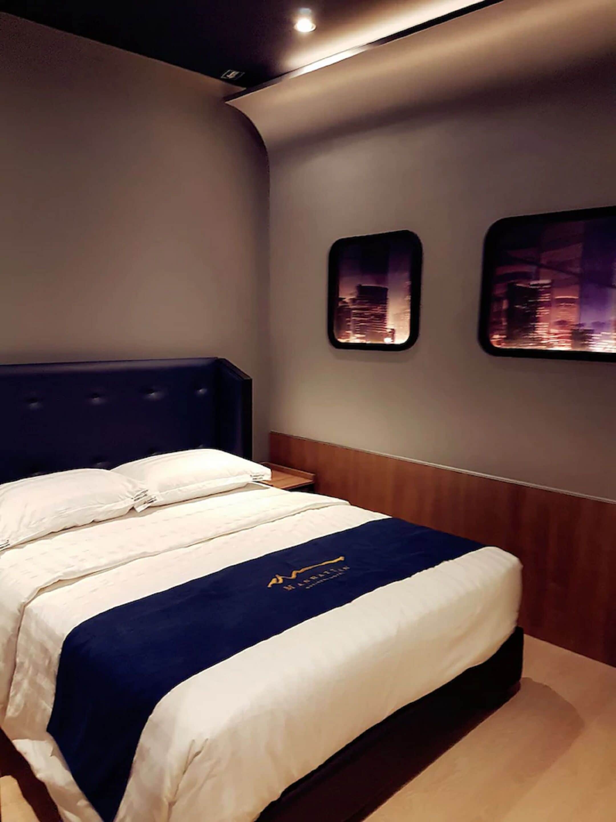 A hotel room with a neatly made bed, a wooden headboard, and two framed pictures on the wall.