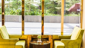 A reception area with two green armchairs, a glass-top table with a small plant, and a view of a green outdoor area through large windows. - Manhattan Business Hotel TTDI (Kuala Lumpur)