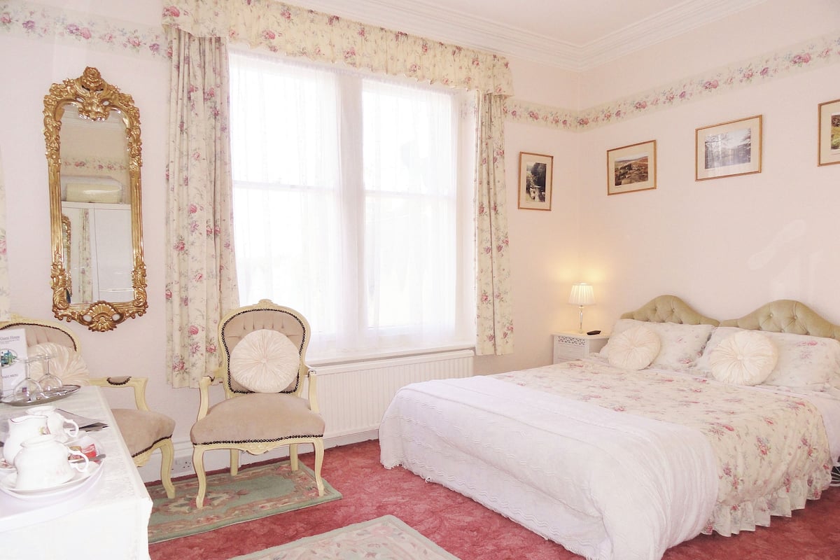 A bedroom with a large bed, a chair, a dresser, a mirror, and a window with curtains.