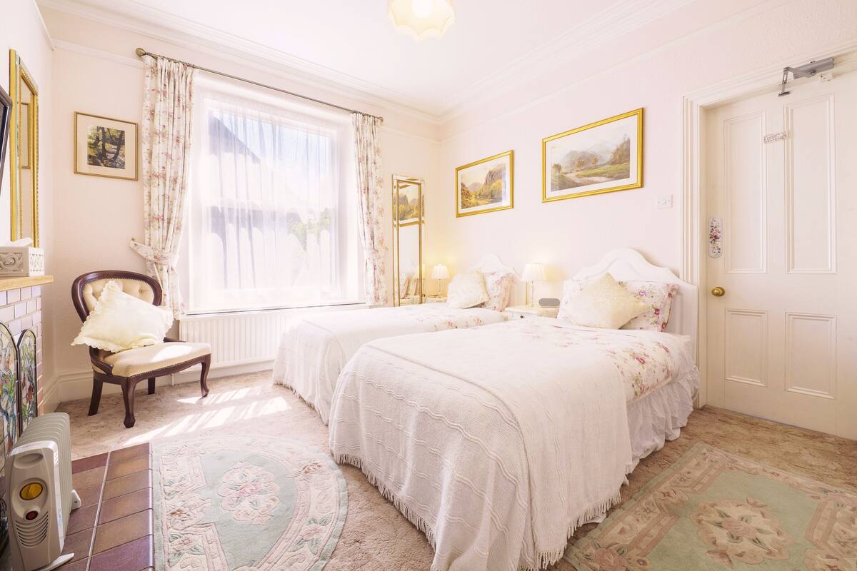 A room with two beds, a chair, a radiator, and a window with curtains.