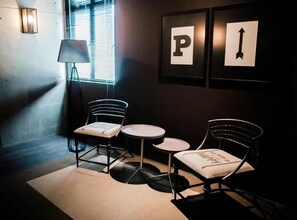A room with two metal-framed chairs, a small round table, a floor lamp, and a window with blinds. There are framed letters 'P' and an arrow on the wall. - M Boutique Kampar (Kampar)