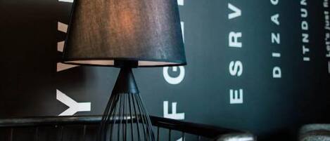 Una lámpara moderna con una pantalla oscura, un soporte de metal negro y un logotipo visible en la pared de fondo.
