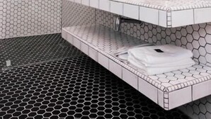 A modern bathroom with hexagonal tile patterns, a glass-enclosed shower, a white sink, and a mirror with a towel rack. - M Boutique Kampar (Kampar)