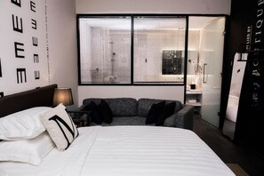 A modern bedroom with a large bed, a gray sofa, and a window with blinds. - M Boutique Kampar (Kampar)