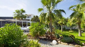 A tropical garden with palm trees, a pool area, and a covered seating area. - Hotel Boutique Ses Pitreras (Sant Josep de sa Talaia)