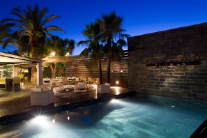 A poolside area with lounge chairs and tables, a stone wall, and palm trees. - Hotel Boutique Ses Pitreras (Sant Josep de sa Talaia)