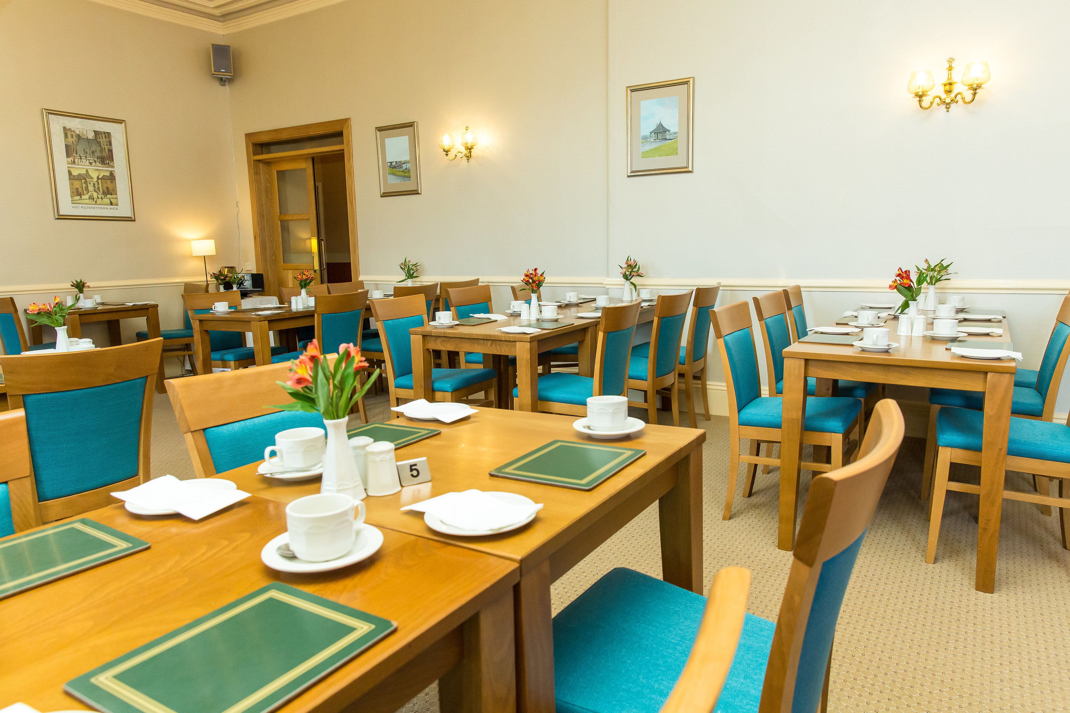 A dining area with multiple tables and chairs, each set with white plates, cups, and cutlery.